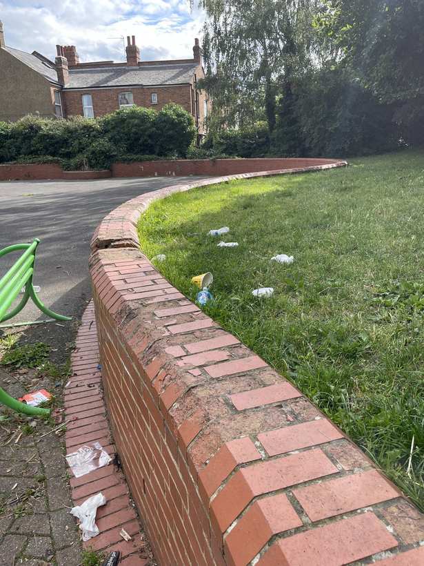 Litter on the grass in front of a cracked, crumbling boundary wall.